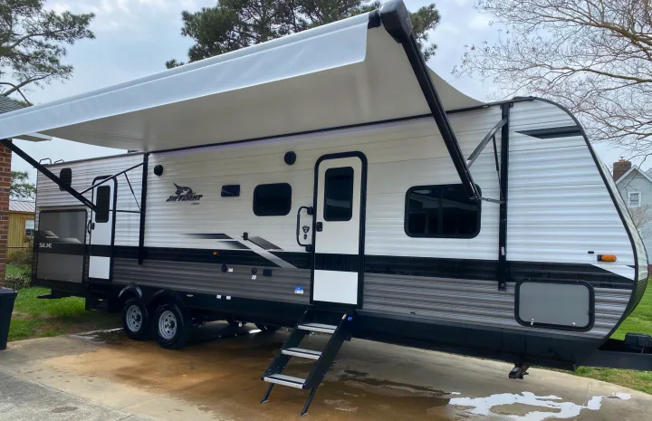 A spacious Jayco travel trailer with an extended awning, parked on a wet driveway, ready for your next RV rental trip.. Jayco Jay Flight SLX 2022