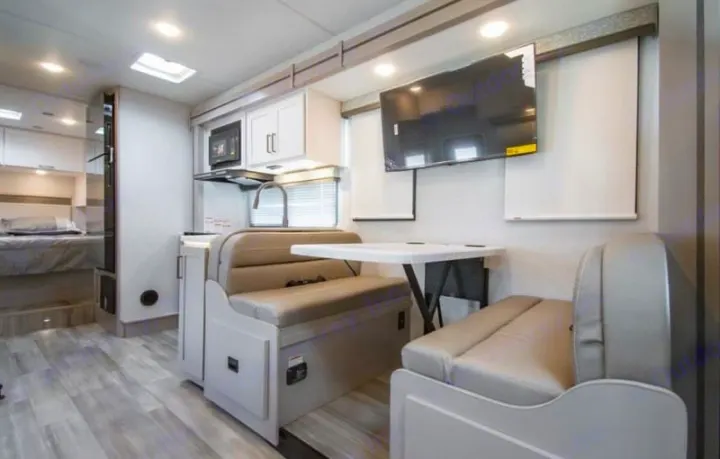 Modern RV rental interior features a cozy dinette, kitchen with microwave/sink, and a glimpse of the bedroom. Ideal for travel.. Thor four winds 2027