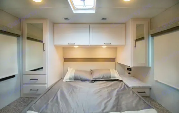 Compact RV rental bedroom interior with a cozy bed, overhead storage, mirrored cabinets, and bedside drawers.. Thor four winds 2027