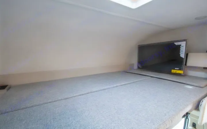 This RV rental interior shows a light-colored sleeping berth with grey cushions and a flat-screen TV on the right for entertainment.. Thor four winds 2027