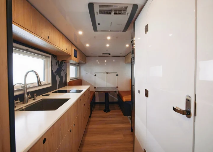 Inside a bright RV rental: a modern kitchen with sink, cooktop, wooden cabinets, and a cozy dining booth.. Storyteller Epic 2025