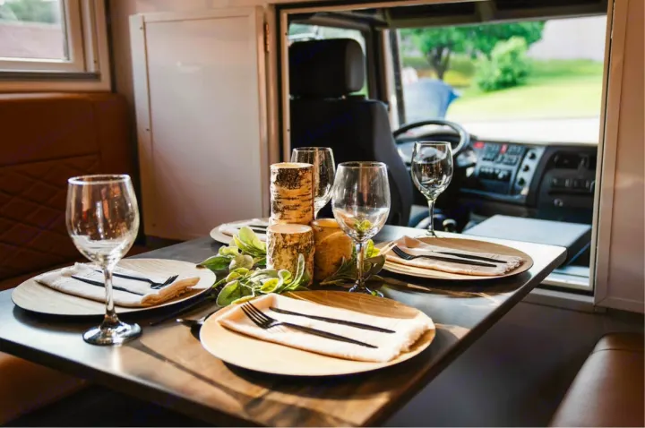 Experience luxury dining in this RV rental. A beautifully set table with wine glasses, birch decor, and a view of the road.. Storyteller Epic 2025