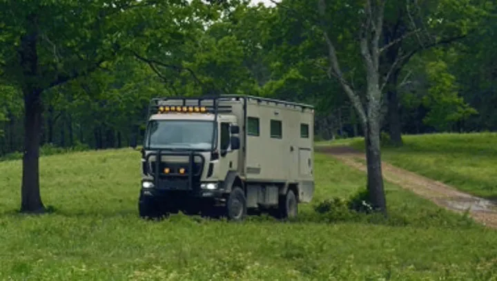 Rugged expedition rv rental, an off-road camper truck, parked in a vibrant green, tree-lined landscape.. Storyteller Epic 2025