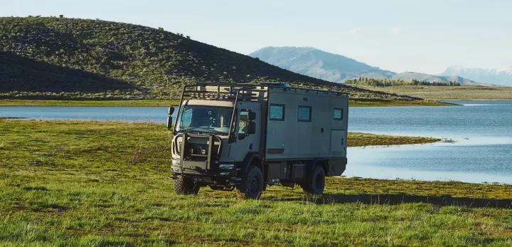 Robust off-road RV rental parked lakeside, perfect for exploring mountains and green hills. An ultimate adventure vehicle.. Storyteller Epic 2025
