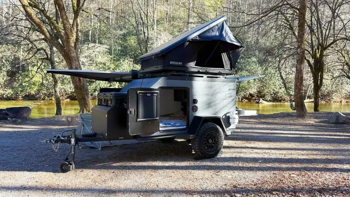 Rugged off-road camper trailer with a rooftop tent and awning, parked by a river – ideal for an rv rental.. Cedar Ridge Deneb XT 2025