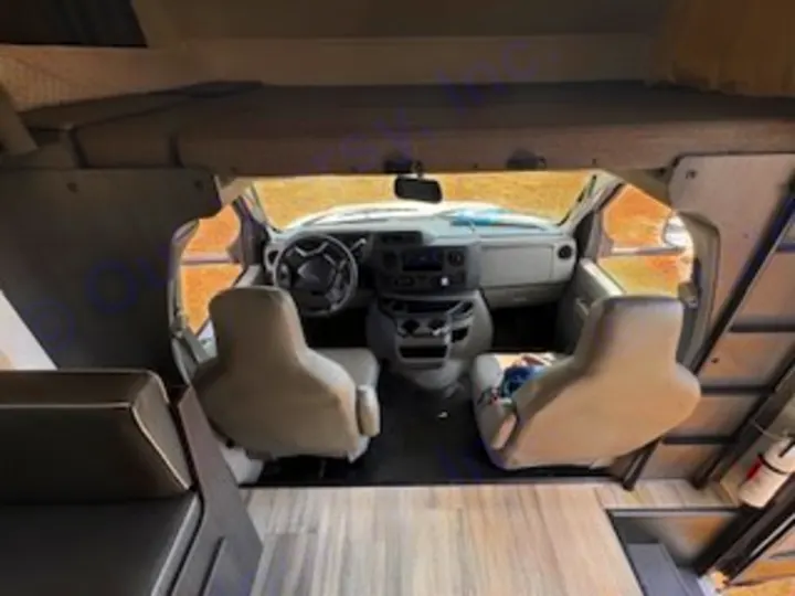 Inside an RV rental: View from the back looking forward at the cockpit, front seats, and overhead bunk area.. Forest River Sunseeker LE 2024