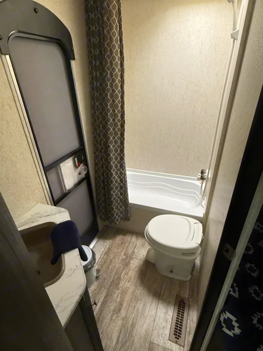 RV rental bathroom: A compact space with a sink, toilet, tub/shower, wood-look floor, and patterned shower curtain.. Highland Ridge RV Open Range 2019