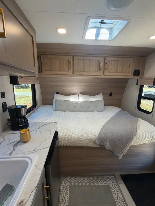 Inside a compact rv rental: bedroom with overhead cabinets, skylight, and a small counter with sink & coffee maker.. KZ Sportsmen Classic 130BH 2026