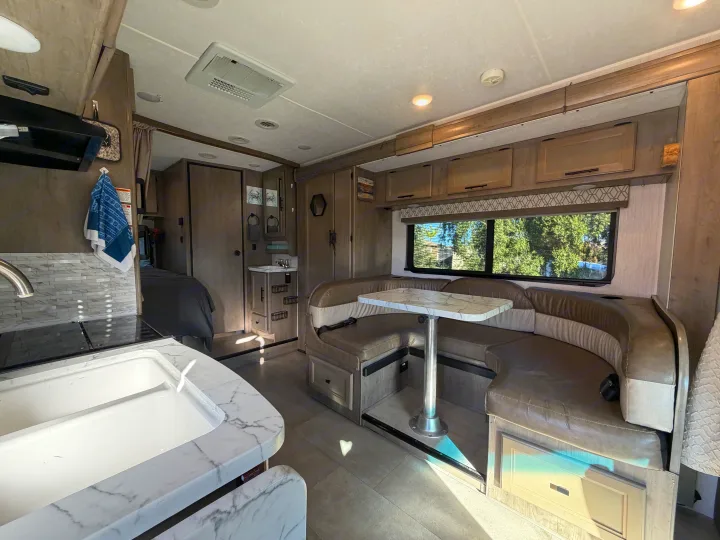 Spacious RV rental interior featuring a kitchen, U-shaped dining booth, bedroom, and bright window view of trees.. Coachmen Other 2020