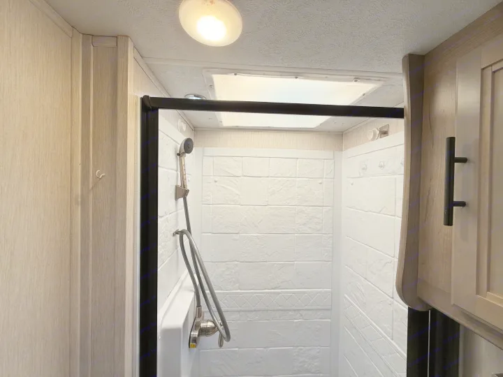 RV rental shower interior: bright white walls with a tile pattern, an adjustable shower head, overhead light, and skylight.. Coachmen Other 2020