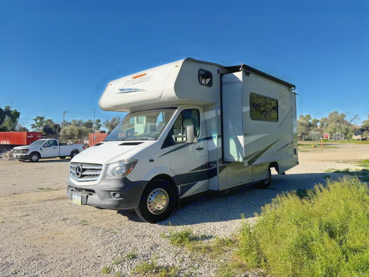 Sunny day showing a white Mercedes Sprinter rv rental on a gravel lot. A pickup and shipping containers are in the distance.. Coachmen Other 2020