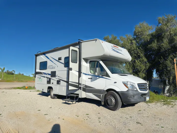 Modern Coachmen Prism Class C RV rental on gravel. White and grey exterior, parked with green hills and trees behind it.. Coachmen Other 2020