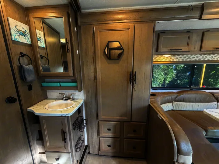 Modern RV rental interior with a light wood-look finish, showing a bathroom vanity, closet, and dinette seating.. Coachmen Other 2020