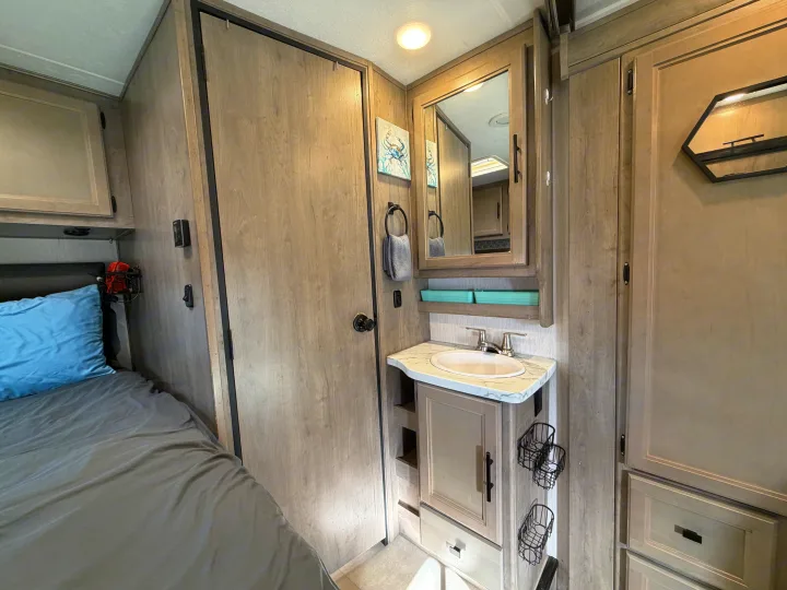 Compact RV rental interior featuring a cozy bed, a small bathroom vanity with a sink, mirror, and cabinet storage.. Coachmen Other 2020
