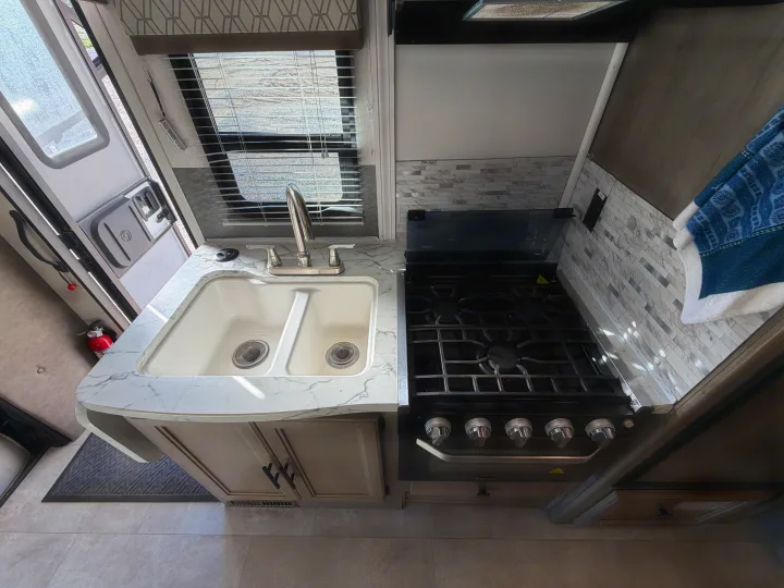 This RV rental kitchen features a double sink, stove, modern backsplash, and counter. Ideal for mobile living.. Coachmen Other 2020