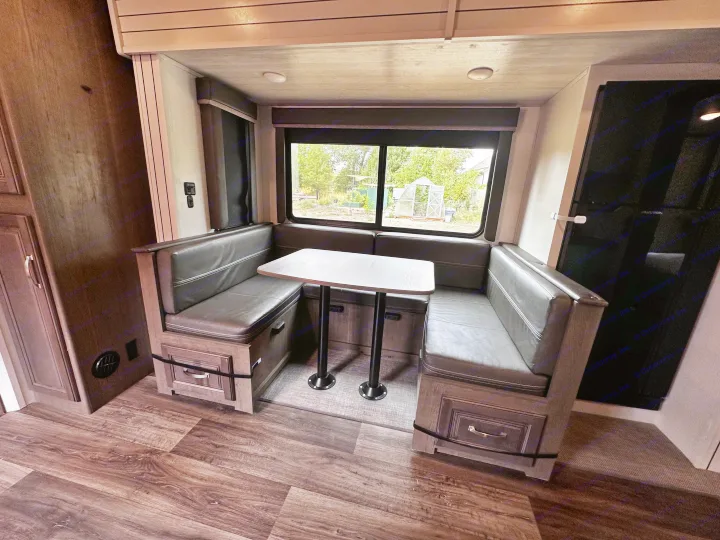 RV rental dinette booth: dark grey cushioned seating, light table, wood-look floor, and window view. Perfect for travel.. Keystone RV Cougar 2023