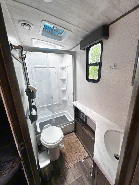 Inside this RV rental, a compact yet complete bathroom with shower, toilet, and vanity sink, perfect for travel comfort.. Keystone RV Cougar 2023