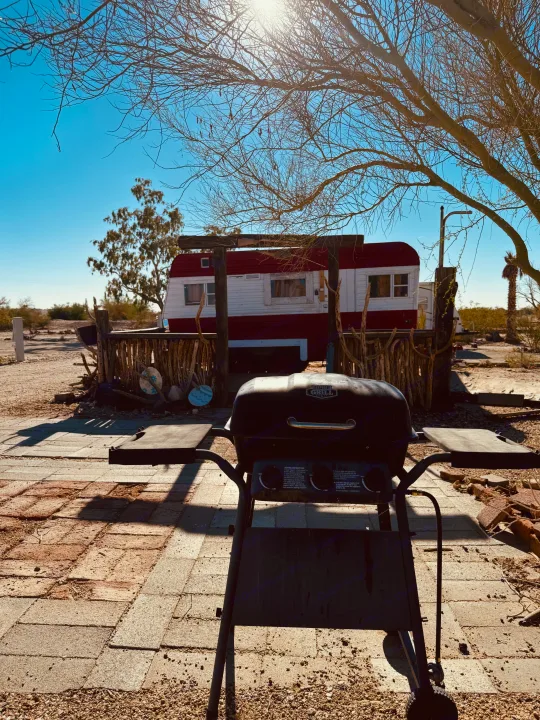RV rental perfect for desert escapes! Features a vintage red & white trailer, BBQ grill on patio, under bright sunny sky and bare trees.. Kit Kit Trailer Deluxe 1978