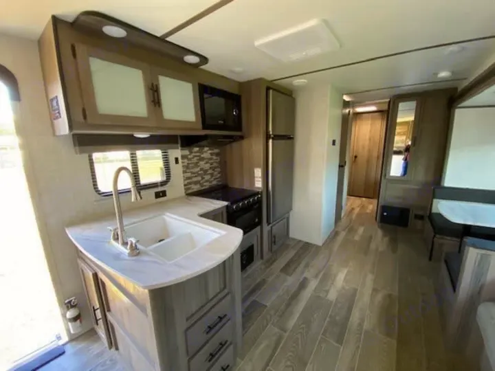 Inside a bright RV rental, a full kitchen with sink, microwave, stove, fridge, and a dinette across the aisle.. Gulf Stream Ameri-Lite 2023