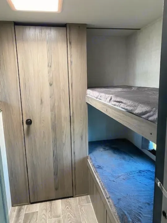 RV rental bedroom features two cozy bunk beds (top grey, bottom blue) and a light wood-grain closet.. Gulf Stream Ameri-Lite 2023