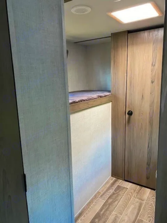 Peek inside an rv rental: compact sleeping area with bunk beds, adjacent wood-look closet, and light flooring.. Gulf Stream Ameri-Lite 2023