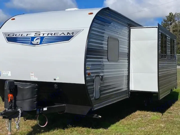 Gulf Stream travel trailer, ideal RV rental. Gray and white with an extended slide-out, parked on grass.. Gulf Stream Ameri-Lite 2023
