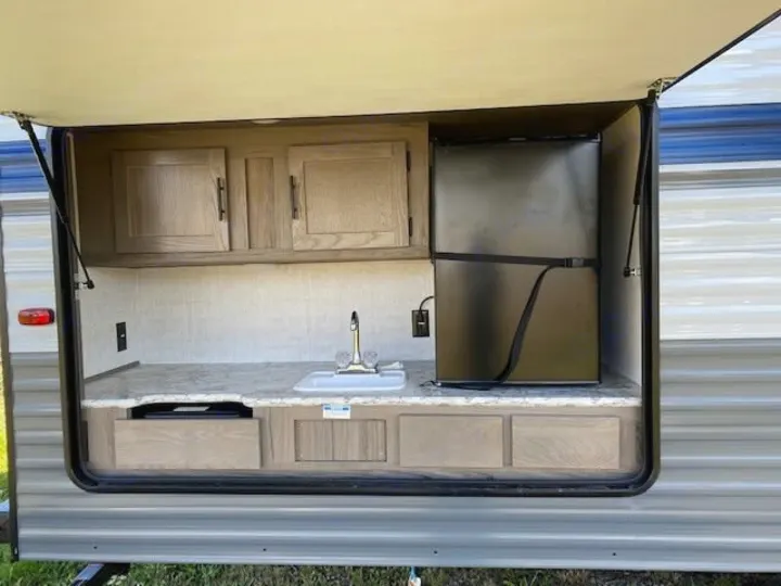 This RV rental's outdoor kitchen features a sink, mini-fridge, and cabinets, perfect for convenient camping and outdoor cooking.. Gulf Stream Ameri-Lite 2023