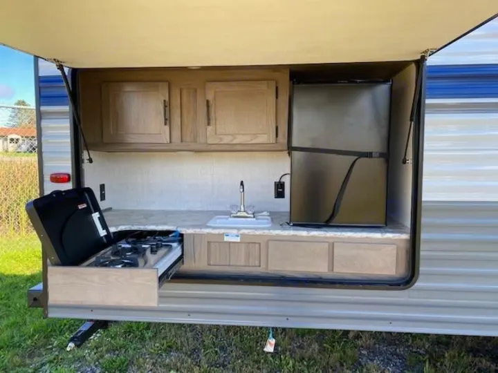 RV rental outdoor kitchen with a pull-out stove, sink, refrigerator, and storage cabinets.. Gulf Stream Ameri-Lite 2023
