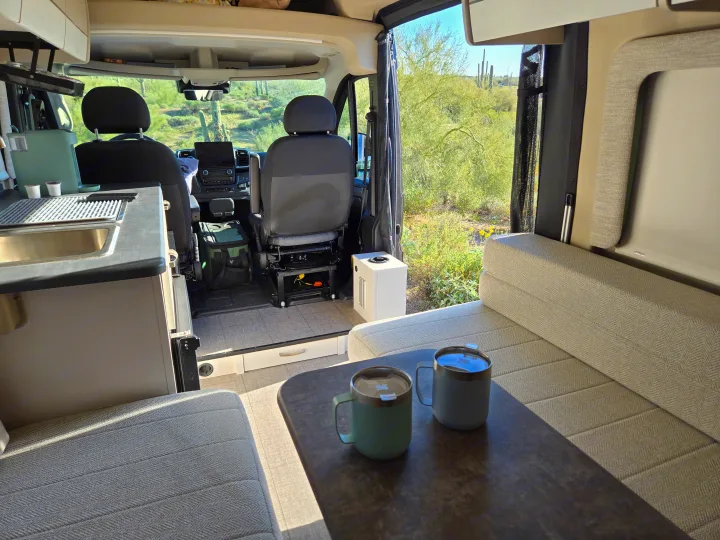 Cozy RV rental interior with desert views, coffee mugs on the table, and a functional kitchen. Perfect for adventure!. Entegra Coach Ethos 2025