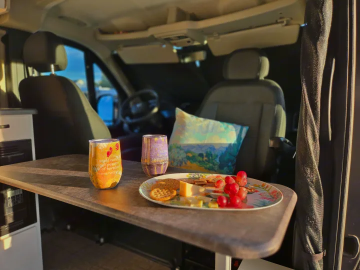 Relaxing in an RV rental: a table with cheese, crackers, grapes, and Van Gogh quote tumblers inside a cozy camper van.. Entegra Coach Ethos 2025