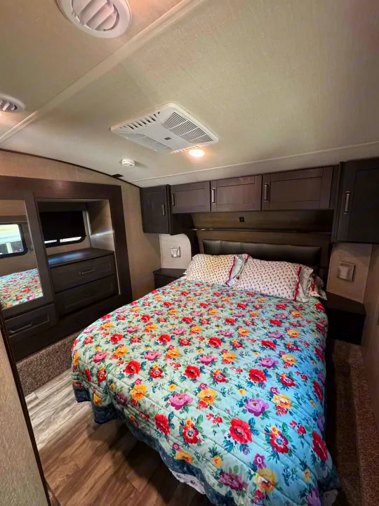 Inside a spacious rv rental bedroom showcasing a bed with a vibrant floral quilt, built-in storage, and AC vents.. Grand Design Reflection 2022