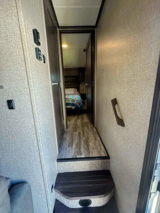 Interior rv rental view: A hallway with steps leading to a bedroom, showing wall controls and a grab handle.. Grand Design Reflection 2022