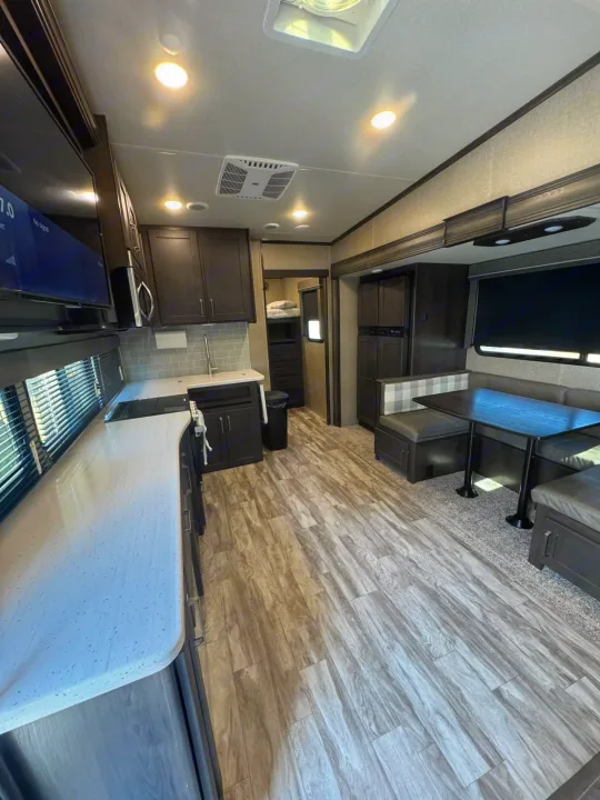 Modern RV rental interior with dark wood cabinets, a light speckled countertop kitchen, and a cozy dinette with checkered cushions.. Grand Design Reflection 2022