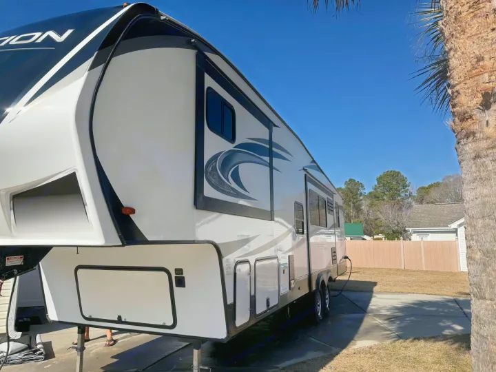 This white and black fifth-wheel RV rental is parked outdoors under a clear blue sky, next to a palm tree, ready for adventure.. Grand Design Reflection 2022