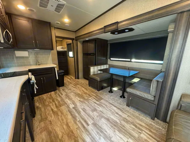 Modern rv rental interior featuring a well-appointed kitchen, booth dinette, and stylish wood-look flooring.. Grand Design Reflection 2022