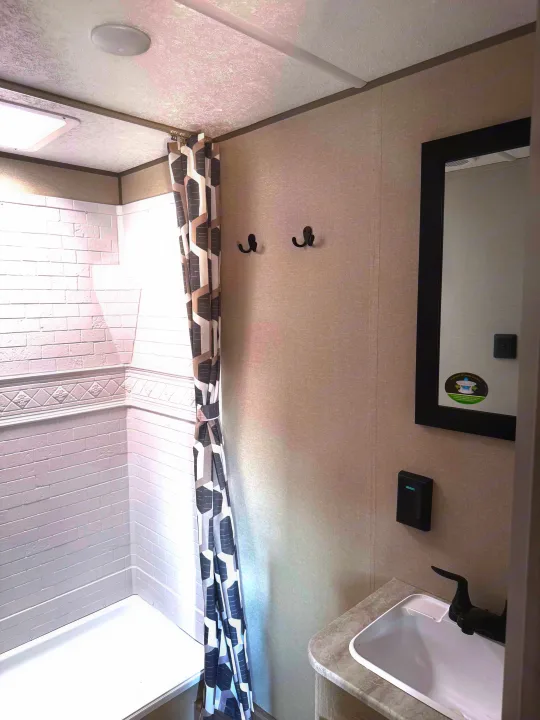 RV rental bathroom: Modern white shower, sink, black faucet, mirror, and hooks. Gray walls & shower curtain.. Coachmen Catalina Sumit 8 2025