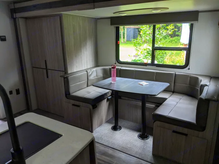 RV rental interior: A U-shaped dinette with a dark table, window views, and a nearby cabinet and partial kitchen area.. Keystone RV Passport SL 2021