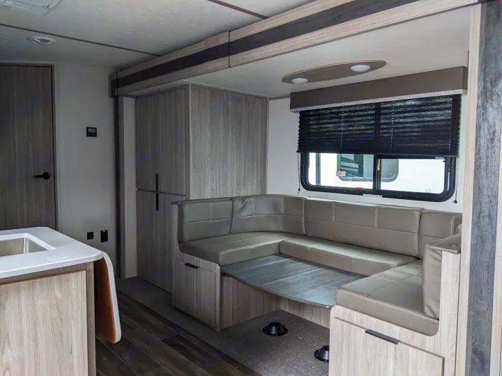 Modern RV rental interior with a U-shaped dinette, kitchen counter, and wood-grain storage for comfortable travels.. Keystone RV Passport SL 2021