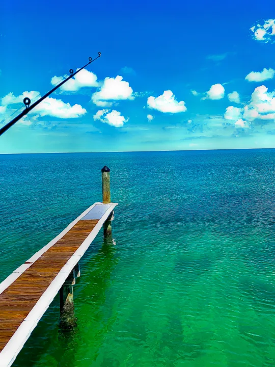 A fishing rod overlooks a wooden pier on crystal clear turquoise waters, with a blue sky. Find this tranquility with an RV rental.. Heartland RVs Pioneer 2022