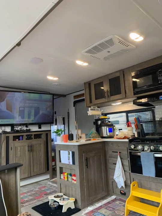 Cozy rv rental living and kitchen area with TV, cooking appliances, and pet food bowls on a patterned rug.. Heartland RVs Pioneer 2022
