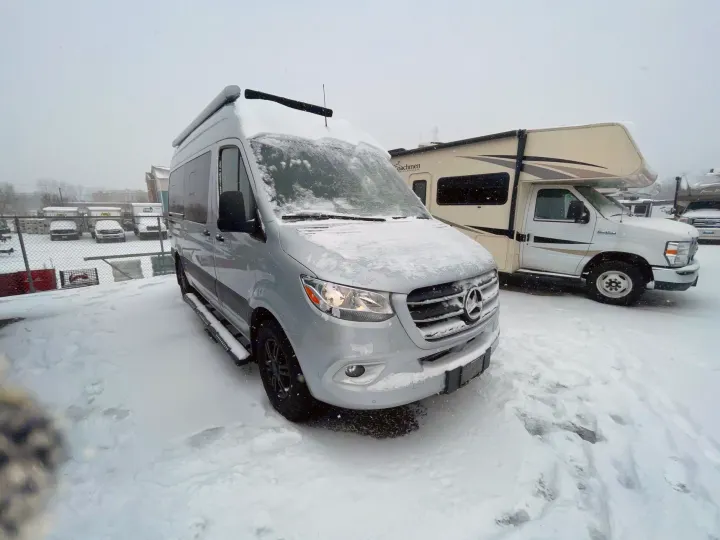 Silver Mercedes Sprinter camper van & Class C RV covered in fresh snow at an RV rental lot. Perfect for winter adventures!. Thor Motor Coach Sprinter 4X4 Tranquility 2023
