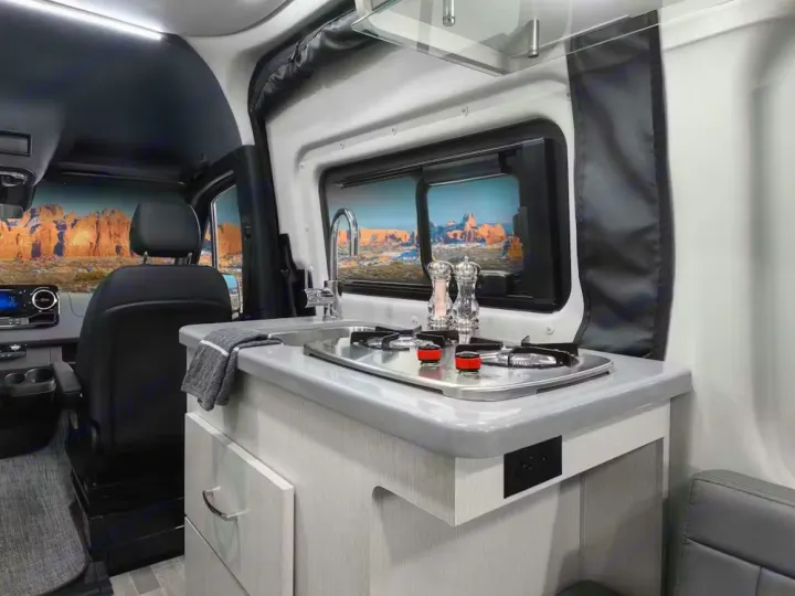 Experience adventure in this RV rental! Features a compact kitchen with stove, sink, and a scenic desert landscape view.. Thor Motor Coach Sprinter 4X4 Tranquility 2023
