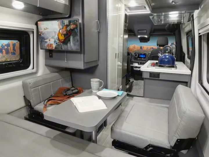 Inside a modern RV rental: a gray camper van interior with a dinette, kitchen area, and TV. Ready for your next adventure!. Thor Motor Coach Sprinter 4X4 Tranquility 2023