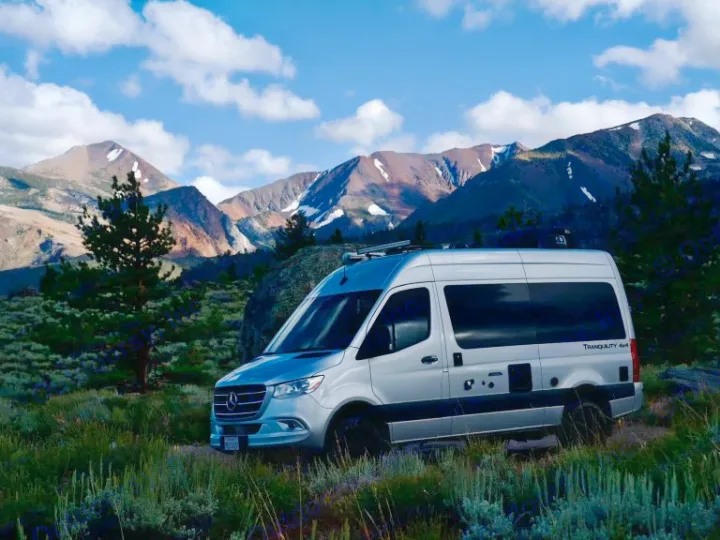 This silver camper van RV rental is perfectly positioned in a scenic mountain landscape with clear skies, ideal for outdoor adventures.. Thor Motor Coach Sprinter 4X4 Tranquility 2023