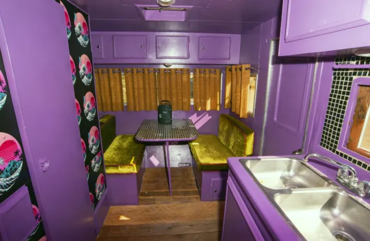 This vibrant purple RV rental interior features a green velvet dinette, kitchenette, and retro vaporwave decor.. Kit Kit Trailer Deluxe 1978