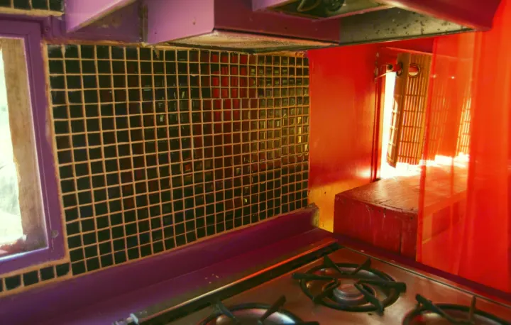 Vibrant RV rental kitchen featuring dark tiled backsplash, purple trim, a stove, and bright red accents.. Kit Kit Trailer Deluxe 1978