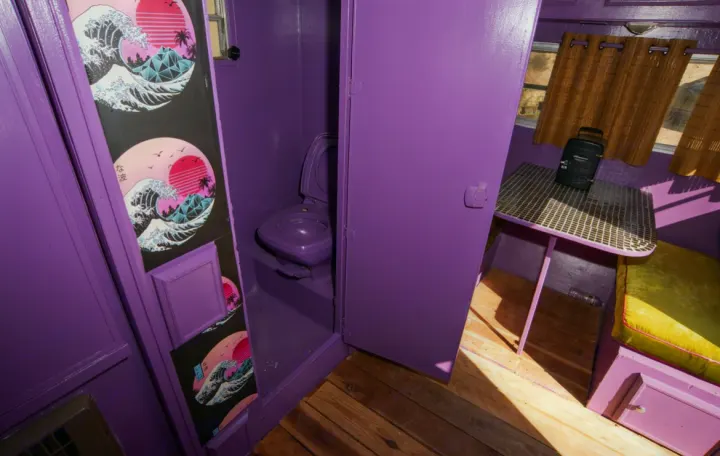 Compact purple RV rental interior: small bathroom with wave art prints, and a dining area with a lime green cushion.. Kit Kit Trailer Deluxe 1978