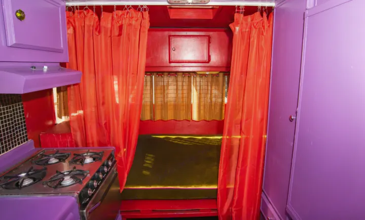 Vibrant purple & red RV rental interior featuring a kitchen stove, bed, and bold decor. Ideal for a colorful road trip.. Kit Kit Trailer Deluxe 1978