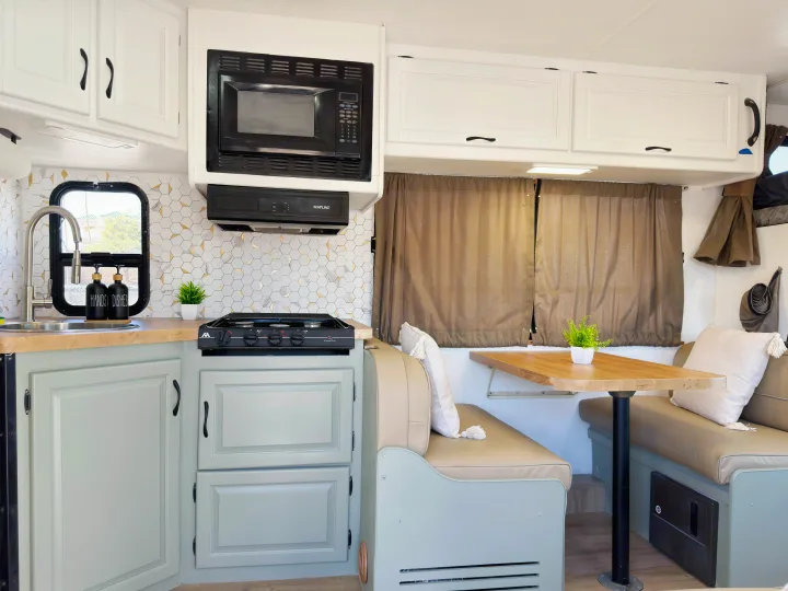 Cozy RV rental kitchen and dinette, featuring white cabinets, hexagonal backsplash, a stovetop, and comfy seating.. Four Winds Majestic 2011