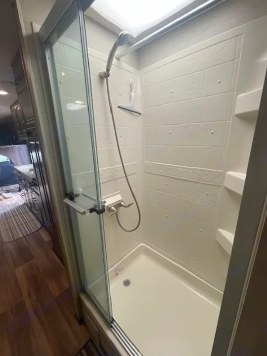 RV rental shower interior: a compact, clean stall with glass doors, handheld showerhead, textured walls, and a skylight.. Jayco Greyhawk 2019